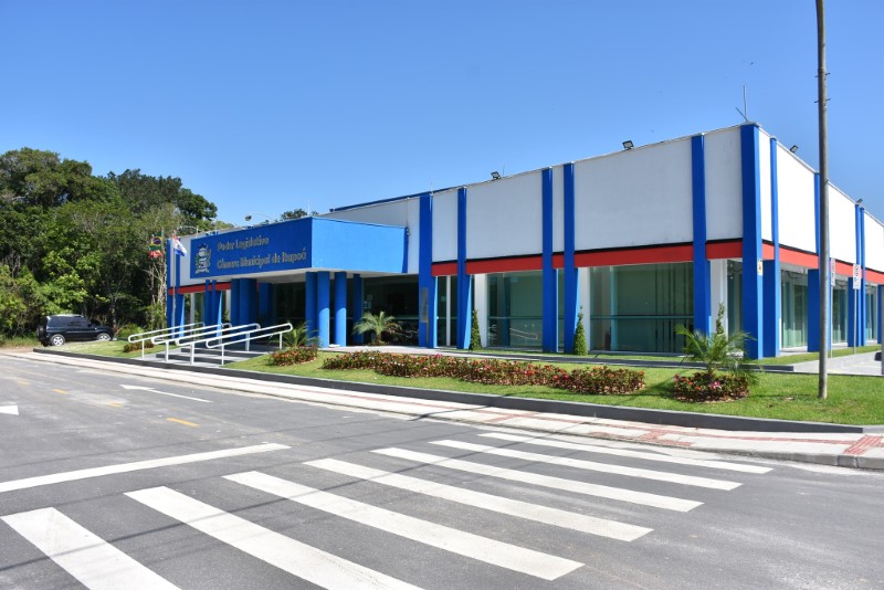 A foto é uma vista externa de um prédio governamental moderno em um dia ensolarado.